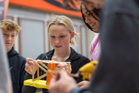 3 students hot gluing popsicle sticks together to make a bridge