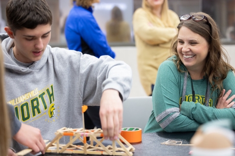 A teacher laughing with her student while taping together a wooden bridge