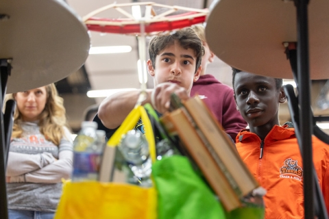 2 students and their teacher looking on nervously as their bridge bends from adding weight